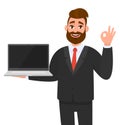 Confident business man holding or showing a new brand, blank screen laptop computer and gesturing, making okay, OK, cool sign. Royalty Free Stock Photo