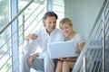 Confident business partners sitting on stairs in office building and discussing work, computer, smiling, mature businessman Royalty Free Stock Photo