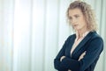 A confident business woman with curly blonde hair standing with her arms crossed in a meeting room Royalty Free Stock Photo