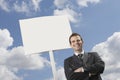 Confident businessman with arms crossed standing by blank sign against cloudy sky Royalty Free Stock Photo