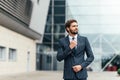 Confident businessman. Confident young man in full suit adjusting his sleeve and looking away while standing outdoors Royalty Free Stock Photo