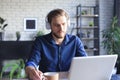 Confident businessman in earphones is writing notes or financial report while sitting at desk with laptop at home Royalty Free Stock Photo