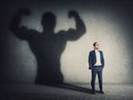 Confident businessman keeps hands in his pockets while casts a powerful person shadow on the wall behind. Business person