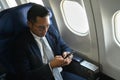 Confident businessman passenger checking news on smart phone, using wireless connection on board during flight