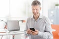 Confident businessman sitting at office desk and connecting with a smartphone, he is using apps and working Royalty Free Stock Photo