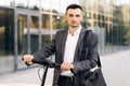 Confident businessman standing with electric scooter and looking at camera. E-Scooter rider rent personal eco transport Royalty Free Stock Photo