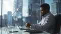 Confident Businessman in Striped Shirt Sitting at a Desk in Modern Office, Using Laptop Computer N Royalty Free Stock Photo