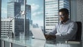 Confident Businessman in Striped Shirt Sitting at a Desk in Modern Office, Using Laptop Computer N Royalty Free Stock Photo