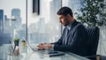 Confident Businessman in a Suit Sitting at a Desk in Modern Office, Using Laptop Computer, Next to Royalty Free Stock Photo