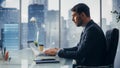 Confident Businessman in a Suit Sitting at a Desk in Modern Office, Using Laptop Computer, Next to Royalty Free Stock Photo