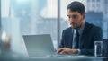 Confident Businessman in a Suit Sitting at a Desk in Modern Office, Using Laptop Computer, Next to Royalty Free Stock Photo