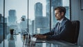 Confident Businessman in a Suit Sitting at a Desk in Modern Office, Using Laptop Computer, Next to Royalty Free Stock Photo