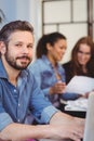 Confident businessman using laptop against female coworkers Royalty Free Stock Photo