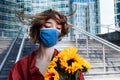 Confident businesswoman in facial mask is awaiting meeting, date, woman with bouquet of sunflowers is standing in financial centre