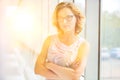 Confident businesswoman standing with arms crossed at new office with yellow lens flare in background Royalty Free Stock Photo