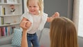 Confident caucasian mother and daughter bonding over giggles while jumping on sofa, radiating joy at their relaxing home