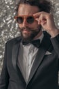 Confident cool bearded guy in black tuxedo arranging sunglasses