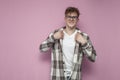 Confident curly guy in glasses straightens his plaid shirt on a pink background and smiles, a man puts on a shirt