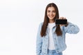 Confident cute brunette female in denim jacket, holding smartphone horizontally, promoting telephone online game or