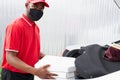 Confident deliveryman in red uniform puts orders in the car