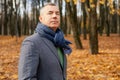 Confident, derisive, tranquil, trendy grizzled modern man in jacket and scarf stand in golden park and look at camera Royalty Free Stock Photo