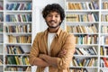 Confident diverse man in casual outfit looking at camera with arms folded on chest on background of closet with books Royalty Free Stock Photo