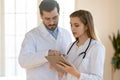 Confident doctor and young nurse talking, working together, using tablet Royalty Free Stock Photo