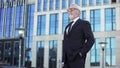 Confident elderly businessman standing outside office building, male director
