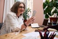 Confident elderly European woman, fashion designer holding watercolor markers while sitting at wooden desk and creating new Royalty Free Stock Photo