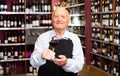 Confident elderly male winemaker inviting to wine house, offering glass of wine for tasting