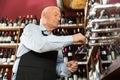 Confident elderly male winemaker pouring wine from wine column in liquor store