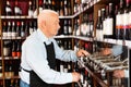 Confident elderly male winemaker pouring wine from wine column in liquor store