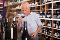 Confident elderly man tasting red wine in wine store before buying Royalty Free Stock Photo