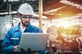 Confident engineer in blue jumpsuit holding laptop computer in a warehouse. Royalty Free Stock Photo