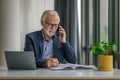 Confident entrepreneur businessman talking on mobile phone while using laptop at business office desk Royalty Free Stock Photo