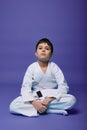 Confident European teenager - aikido fighter - in white kimono sitting in lotus pose while practicing oriental martial arts on