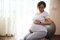 Confident expectant mother, gravid woman touching her pregnant belly, feeling baby kicks, sitting in hero pose on a mat