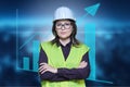 Factory engineer woman in safety helmet vest posing on industrial background with graphs