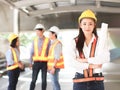 Female architect or engineer holding blue print paper, standing in front of her team smiling and looking at camera Royalty Free Stock Photo