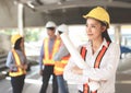 Female architect or engineer holding blue print paper, standing in front of her team smiling and looking sideway Royalty Free Stock Photo