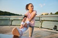 Confident female athlete, determined sportswoman, runner, jogger looking aside while stretching her leg muscles while doing