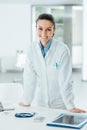 Confident female doctor leaning on desk