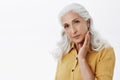 Confident and feminine elegant elderly woman with long white hair in stylish yellow trench coat touching face gently and