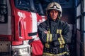 A confident fireman wearing protective uniform standing next to a fire engine in a garage of a fire department, crossed Royalty Free Stock Photo