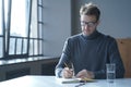 Confident focused German man freelancer in glasses taking notes in agenda sitting at desk at home Royalty Free Stock Photo