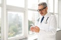 Experienced confident senior doctor with grey hair using smartphone
