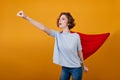 Confident girl in red mantle having fun during photoshoot in studio. Brave young woman in superhero attire waiting for