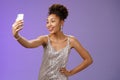 Confident glad attractive stylish millennial african-american woman in silver glittering dress taking selfie posing cute