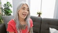 Confident, grey-haired, middle age woman beaming with joy, sitting relaxed on a cozy sofa, engaged in a cheerful conversation at