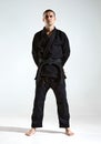 Confident guy in black kimono fighter posing in karate stance on studio background with copy space Royalty Free Stock Photo